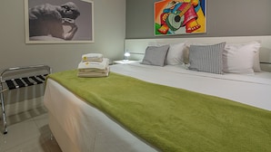 A hotel room with a bed, pillows, a green blanket, a chair, a painting, and a lamp. - 3 Minutos Da Praia De Copacabana | Stc303 (Rio de Janeiro)
