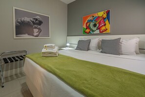 Ein Hotelzimmer mit Bett, Kissen, einer grünen Decke, einem Sessel, einem Gemälde und einer Lampe.