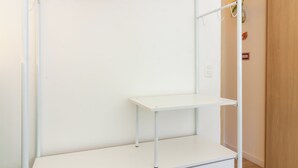 A white metal wardrobe with shelves and a hanging rod, located in a room with wooden flooring and a door in the background. - Aconchegante A Poucos Minutos Da Lagoa | Vlp412 (Rio de Janeiro)