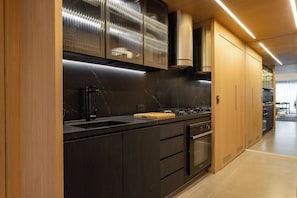 Une cuisine moderne avec des meubles de couleur sombre, un plan de travail noir, une hotte en acier inoxydable et un four encastré.