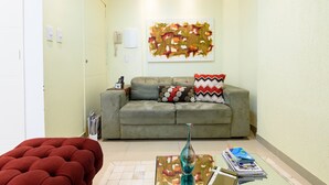 Ein Wohnzimmer mit grauem Sofa, einem roten Hocker, einem Glastisch und einem an der Wand hängenden abstrakten Gemälde.