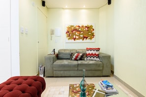 A living room with a grey sofa, red ottoman, and a glass coffee table with magazines.