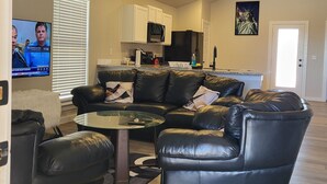 A living room with a black leather sectional sofa, a glass coffee table, and a ceiling fan.