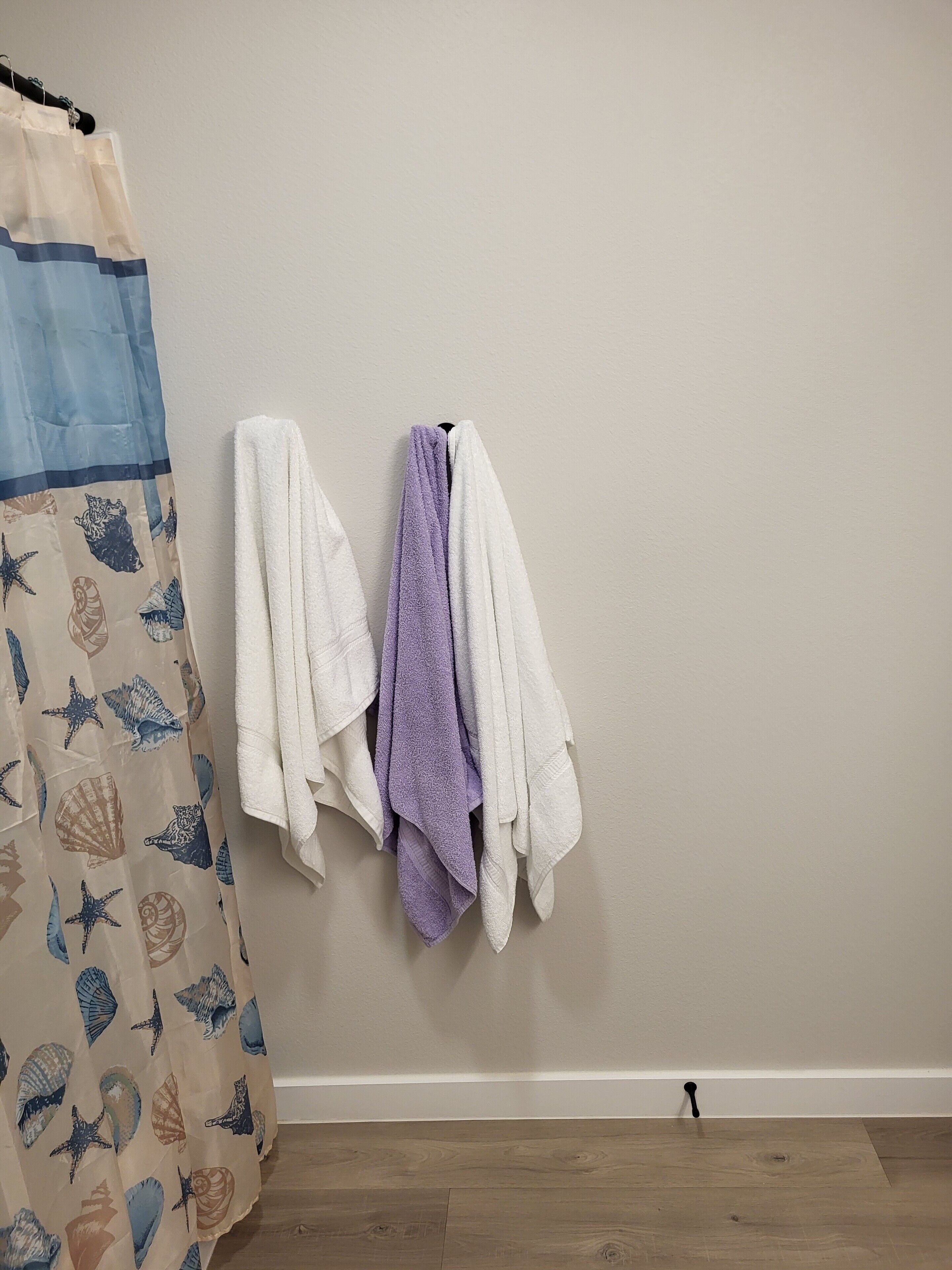 Un bagno con pavimento in legno, parete beige e tenda da doccia con motivo di conchiglie.