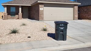 A single-story house with a garage, numbered 513, and a black trash bin labeled 513.