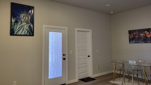 A room with a glass table and chairs, a door with frosted glass, and two wall-mounted paintings.