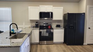 A modern kitchen with white cabinets, a stainless steel oven, a black refrigerator, and a microwave.