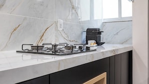 A modern kitchen with a gas stove, a microwave, and a coffee maker on a marble countertop. - Perfeito Para Casais Em Ipanema | Vp802 (Rio de Janeiro)