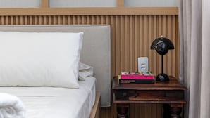 A neatly made bed with white linens, a wooden headboard, a bedside table with a lamp, and a small stack of books. - Perfeito Para Casais Em Ipanema | Vp802 (Rio de Janeiro)