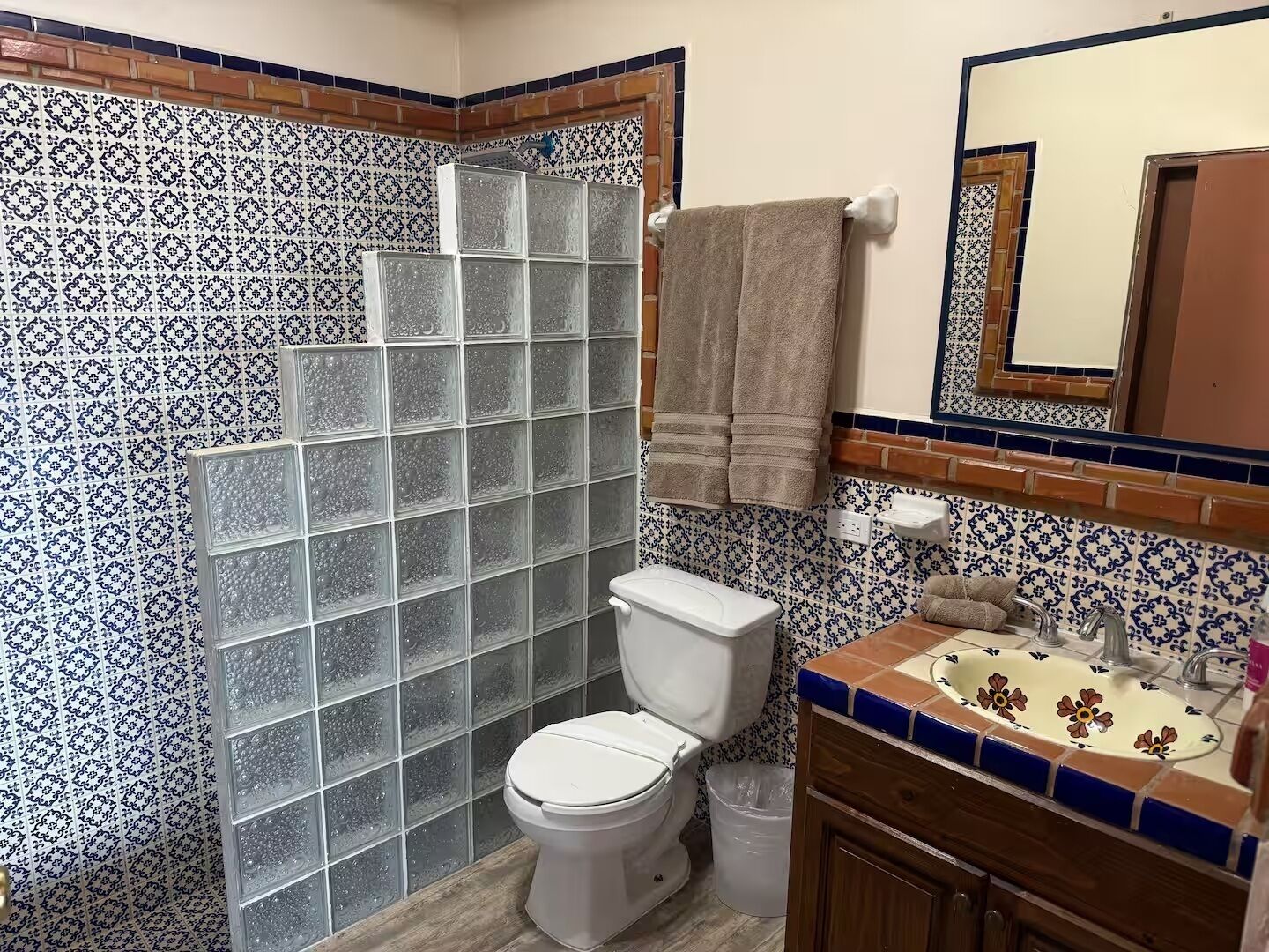 Une salle de bain avec un mur recouvert de carreaux décoratifs, une douche en verre, des toilettes, un lavabo orné de motifs floraux et un meuble en bois.