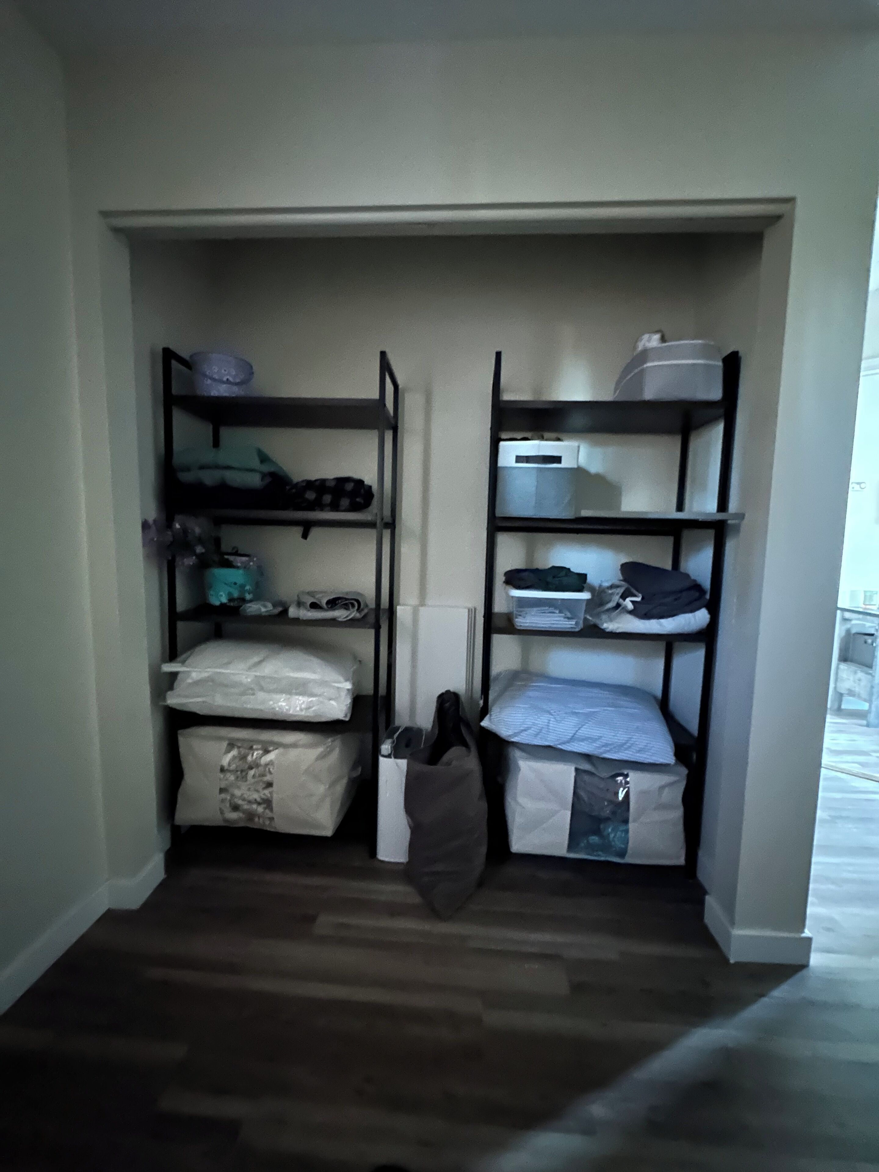 Un meuble de rangement compact doté de plusieurs étagères, dont certaines contiennent des couvertures et des sacs pliés, et d’une petite porte située en bas.