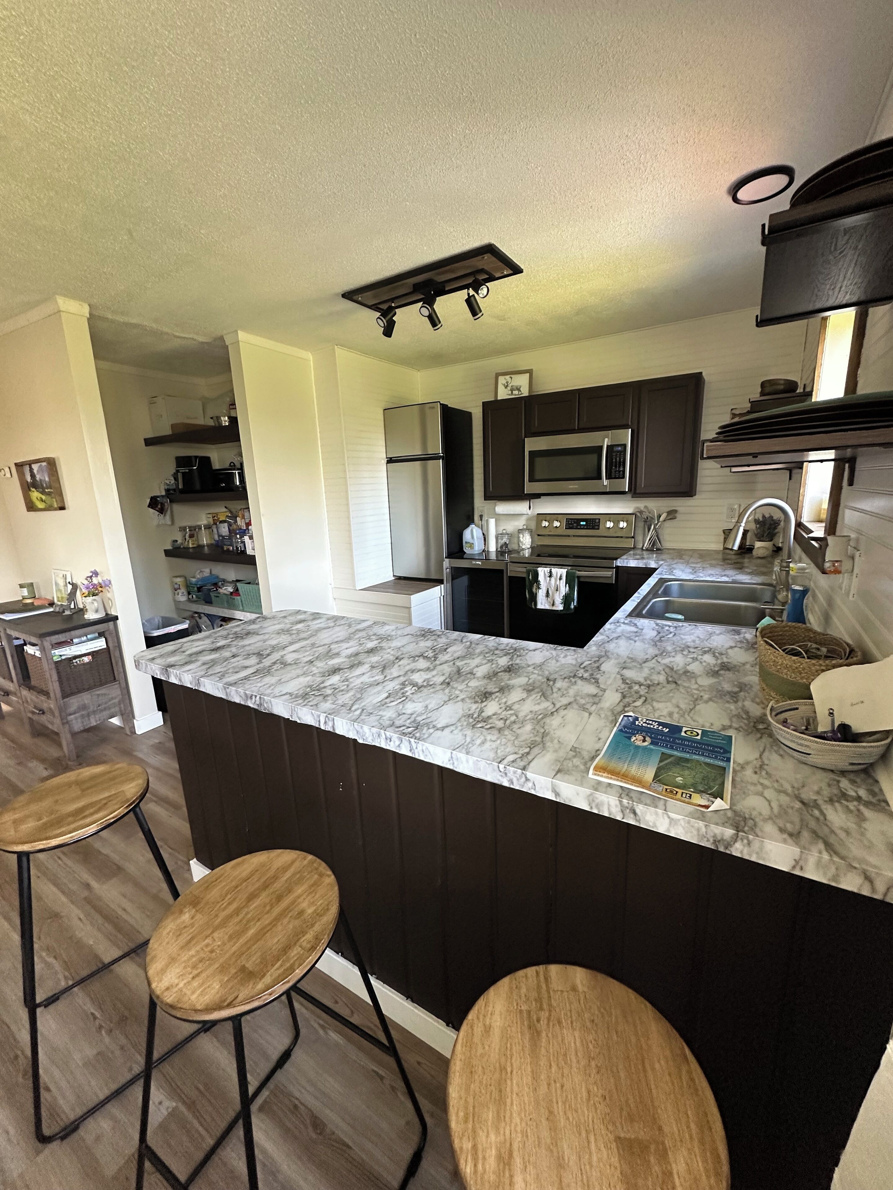 A modern kitchen with a marble countertop, dark cabinetry, and a built-in island with bar stools.