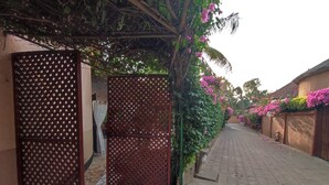 A narrow paved pathway flanked by walls adorned with flowering plants and a decorative metal gate. - Villa pool, residence pools, beach, seaside, beach restaurant (Saly,Région de Thiès)