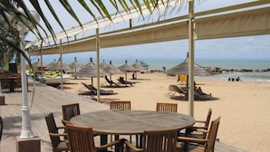 A beachside restaurant with outdoor seating, including a round table and chairs, and thatched umbrellas. - Villa pool, residence pools, beach, seaside, beach restaurant (Saly,Région de Thiès)