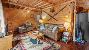 Ein gemütliches Blockhaus-Interieur mit Holzbalkendecke, einer Sofagarnitur, einem Couchtisch, einer Lampe und einem Staubsauger.