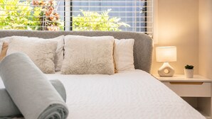 A neatly made bed with a rolled towel, a bedside lamp, and a small potted plant on a bedside table.
