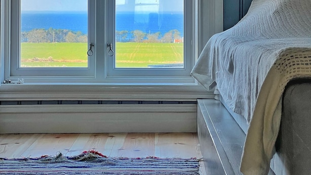 Ein Schlafzimmer mit großem Fenster mit Blick auf ein grünes Feld und den Ozean.