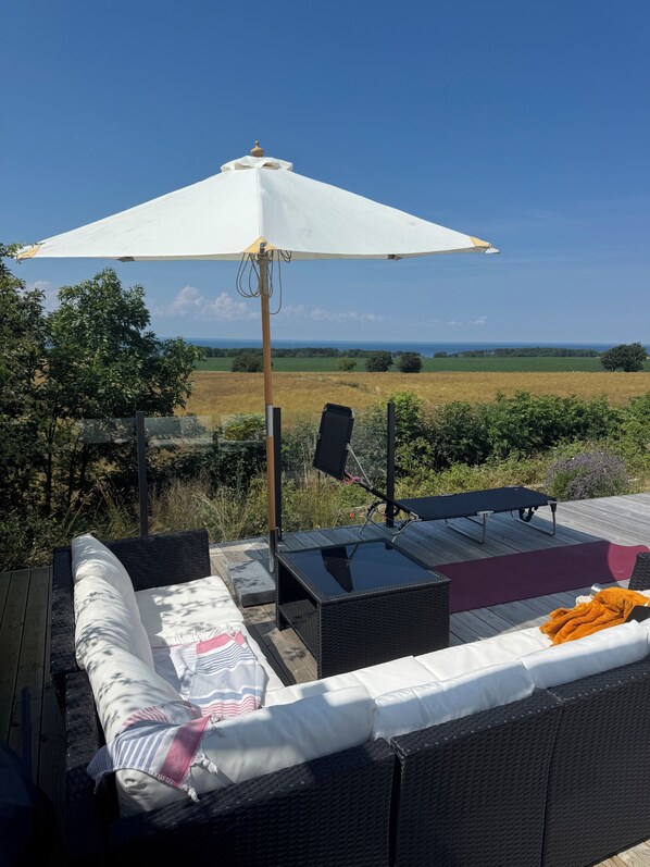 A deck with outdoor furniture, a white umbrella, and a view of the countryside.