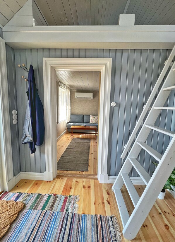 A room with a wooden floor, a sofa, a coffee table, a staircase, and a hanging coat rack. - Newly renovated turn of the century house with sea view close to nature! (Degerhamn)