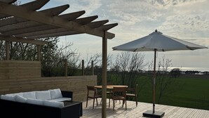 Eine Holzterrasse mit Pergola, Gartenmöbeln und einem Tisch mit Stühlen.
