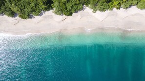 An aerial view of a beach with clear turquoise waters and a sandy shoreline.