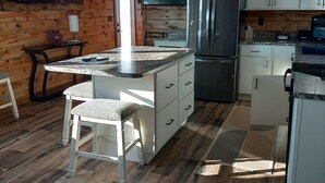 Une cuisine dotée d’un îlot central, de murs en bois, d’un réfrigérateur en acier inoxydable et d’une horloge murale.