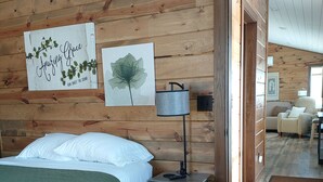 Une chambre confortable avec un plafond en bois, un lit recouvert d’une couverture verte, une table de chevet avec une lampe et des œuvres d’art accrochées au mur.