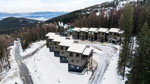 Ein modernes Mehrstöckiges Hotel mit Parkplatz für Skifahrer, umgeben von verschneiterten Flächen und dichtem Wald.