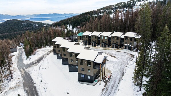 A modern multi-story hotel with a ski slope parking area, surrounded by snow-covered terrain and dense forest.