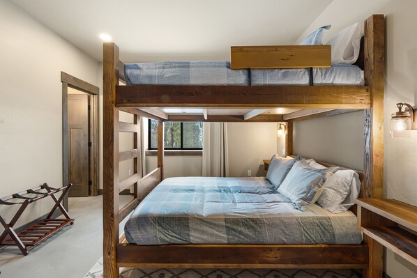A bunk bed with a wooden frame, a bed with a blue and white patterned bedspread, and a small bedside table with a lamp.
