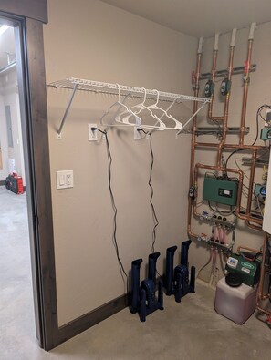 A room with a metal rack, electrical outlets, copper pipes, and a green water heater.