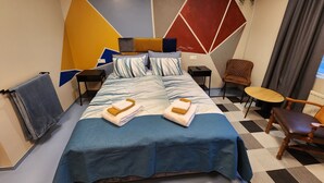 A modern hotel room with a large bed, a desk, a chair, and a small table.