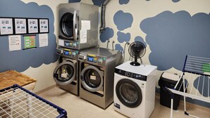 A laundry room with multiple washing machines, a dryer, a fan, and a clothes drying rack.