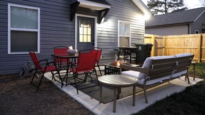 Een terras buiten met een tafel, stoelen, een bank en een barbecue.