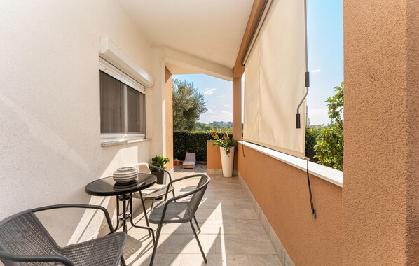 A balcony with a table and chairs, a window, and a view of greenery and buildings.