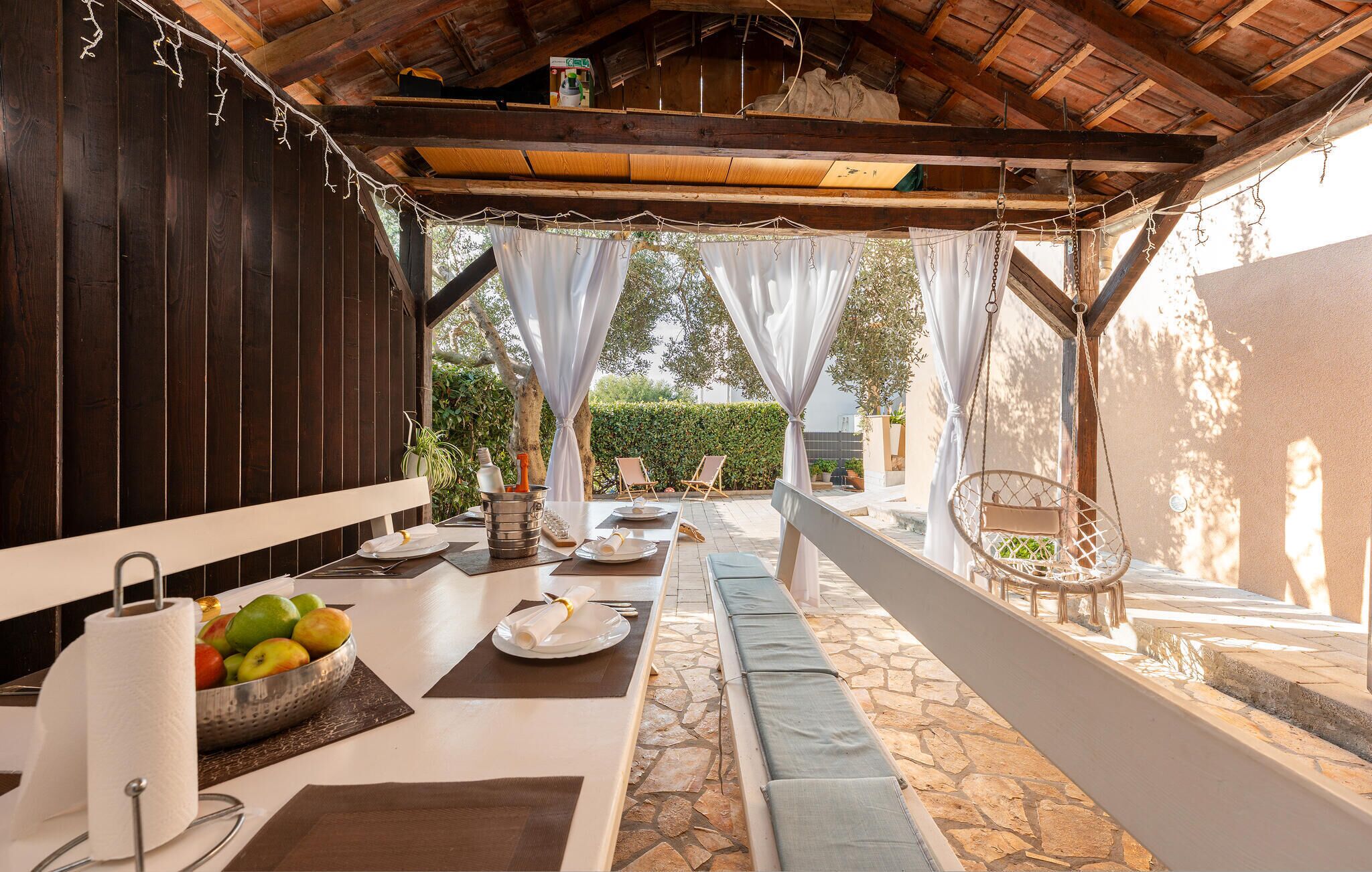 Un espacio exterior para comer con piso de piedra, vigas de madera y luces de macramé colgantes.