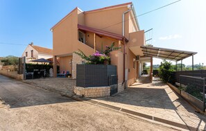 A modern two-story house with a stone facade, a covered patio, and a gated entrance.