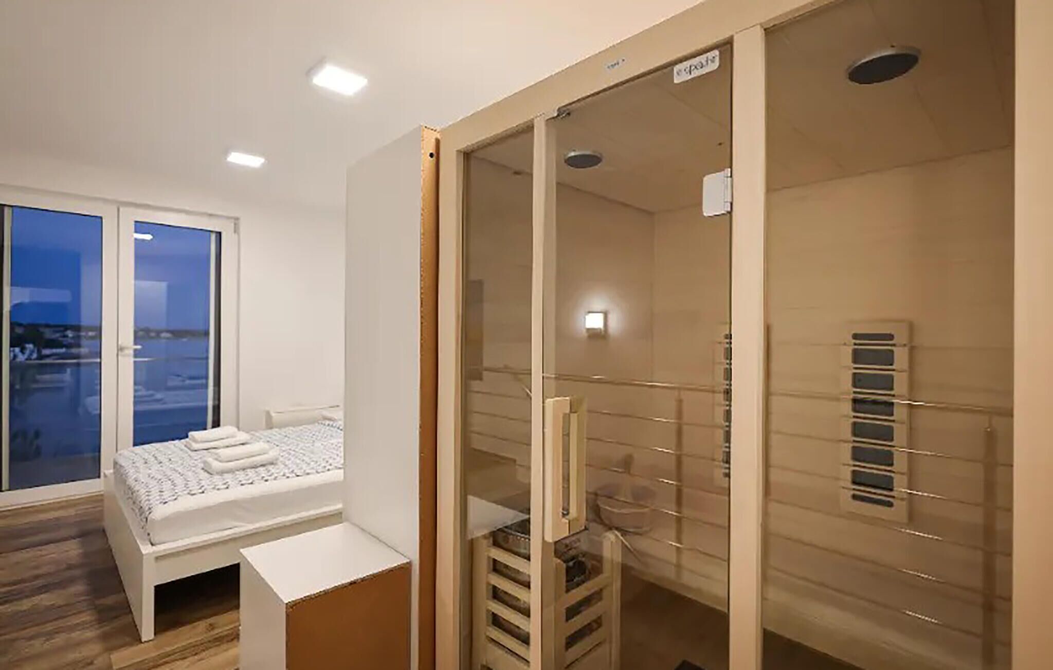 Et soveværelse med en seng, et lille bord, en glas brusekabine og udsigt ud