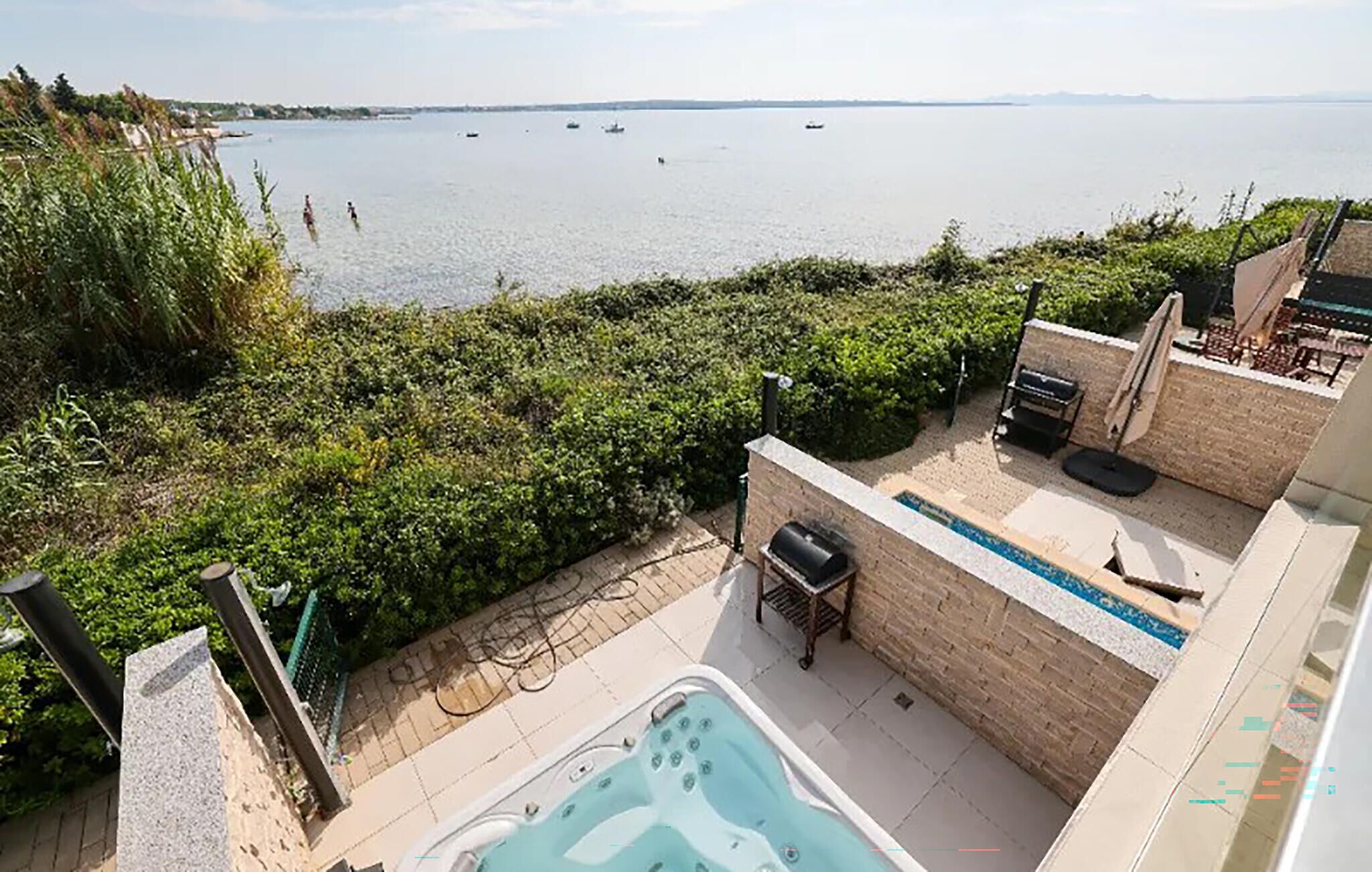 Ein Poolbereich mit Whirlpool, Grillmöglichkeit und Blick auf einen See mit Booten.