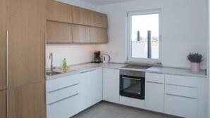 A modern kitchen with white cabinets, a built-in oven, a window, and a small potted plant.