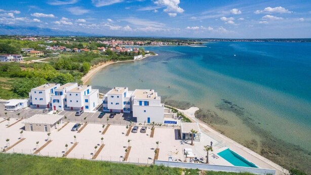 A coastal hotel with a parking lot, a swimming pool, and a view of the sea.