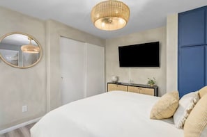 Un dormitorio con cama, televisor montado en la pared, espejo y armario.