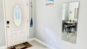 A hallway with a white door, a small rug, a painting, and a mirror reflecting a dining area. - The Blue Oasis, a beach-themed Florida getaway (Tampa)