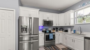 A modern kitchen with white cabinets, stainless steel appliances, and a window with a view of greenery. - The Blue Oasis, a beach-themed Florida getaway (Tampa)