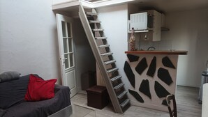 A compact living space with a staircase leading to a kitchen area, a small table, and a couch with a red pillow.
