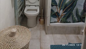 A bathroom with a toilet, shelves with towels, a shower curtain with a tropical design, and a woven basket.