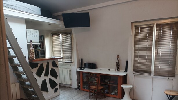 A compact living space with a staircase, a small kitchen area, and a seating area with a sofa and a table.