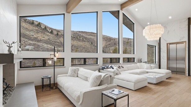 A spacious living room with large windows, a fireplace, and a modern chandelier.