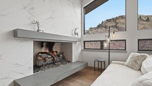 A modern living room with a fireplace, marble walls, and large windows offering a mountain view.