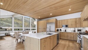 A modern kitchen with wooden cabinets, a large island, and a dining area with a view of the outdoors.